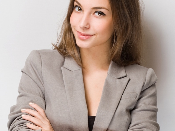 Confident woman in a gray blazer with arms crossed, smiling gently.