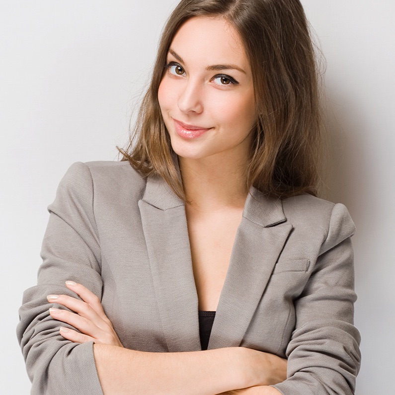 Confident woman in a gray blazer with arms crossed, smiling gently.