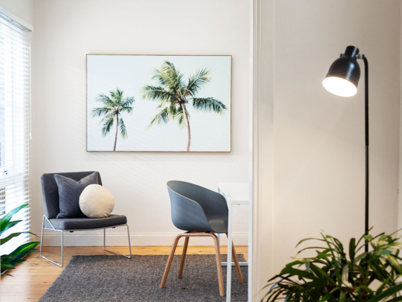 Modern room with blue chairs, plant, and palm tree wall art.