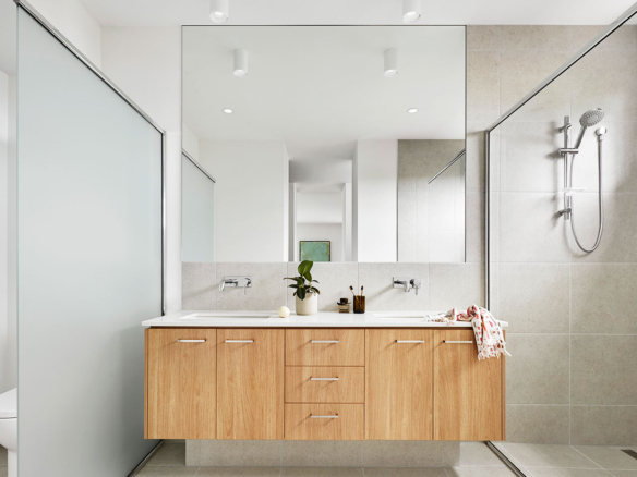 Modern bathroom with wooden vanity and dual sinks under large mirrors.