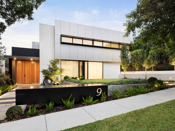 Modern white house with large windows and landscaped front yard.