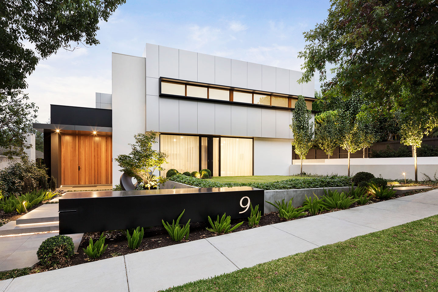 Modern white house with large windows and landscaped front yard.