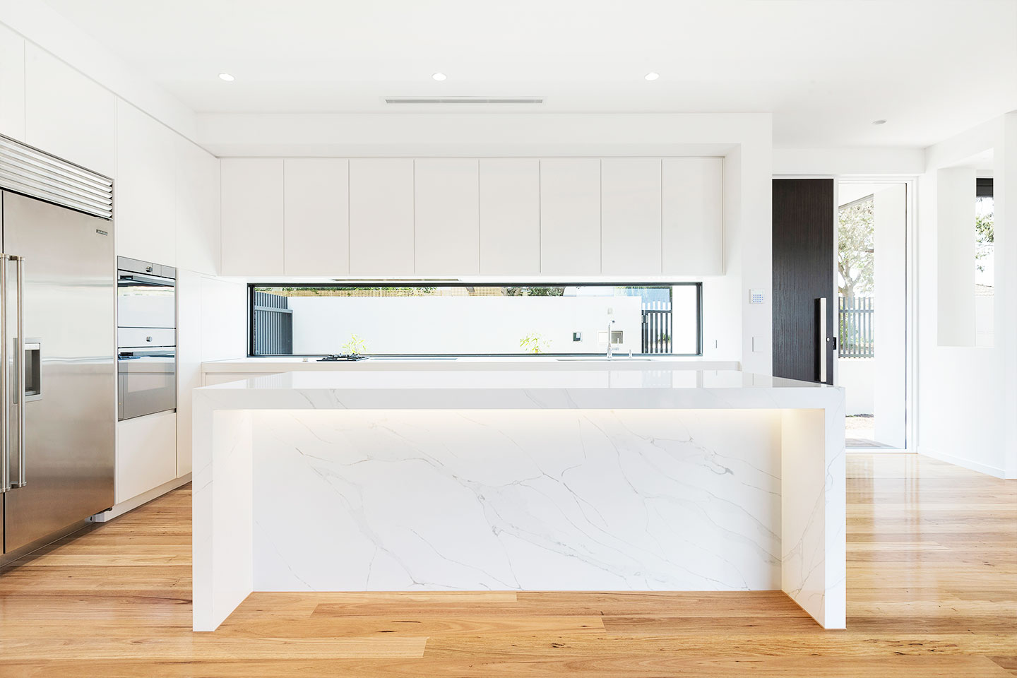 Modern kitchen island with white marble and wooden flooring.