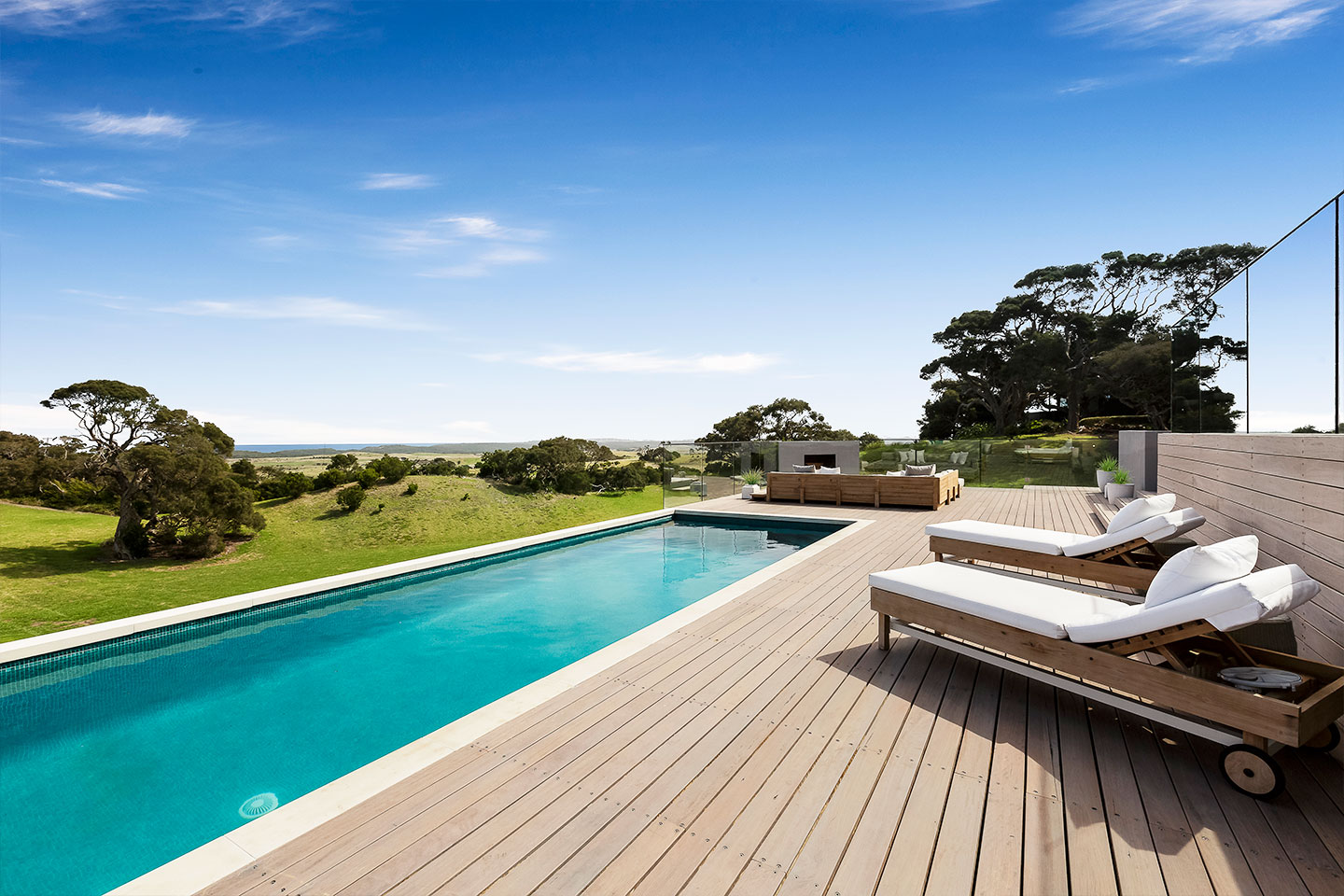 Modern outdoor pool with loungers and scenic green landscape.