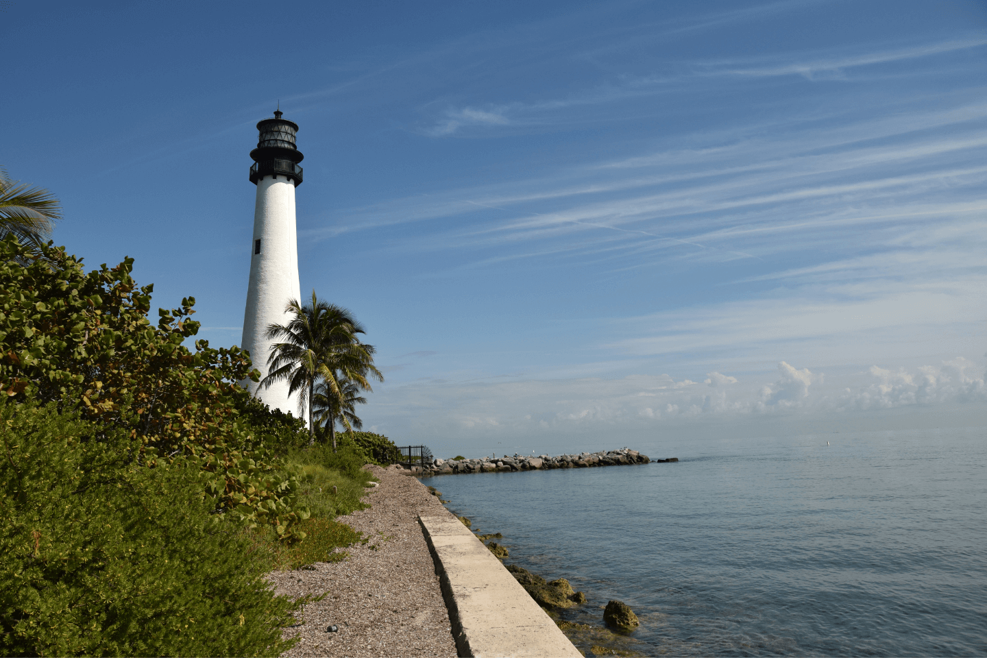 A lighthouse stands tall near a calm sea under a blue sky.