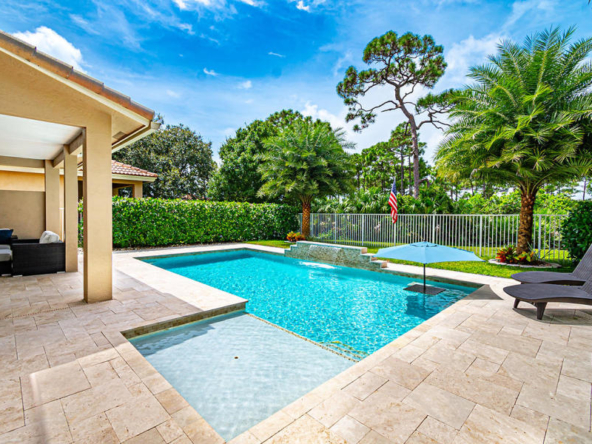 A modern backyard pool with clear blue water and surrounding greenery.