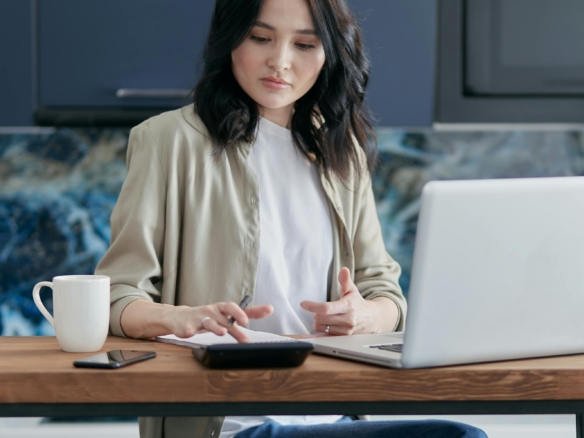 Young woman working on a laptop at a table with a coffee mug nearby.