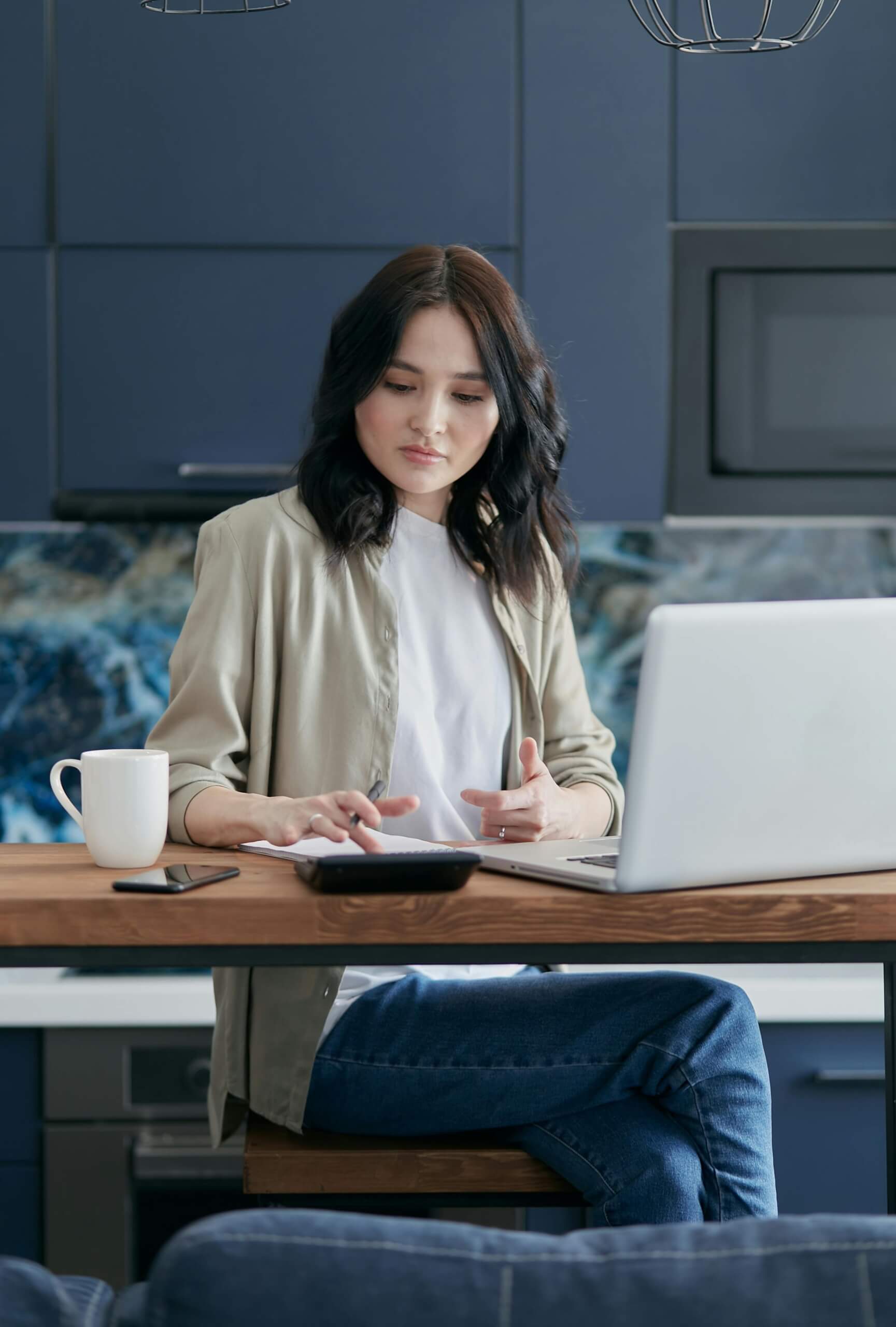 Young woman working on a laptop at a table with a coffee mug nearby.