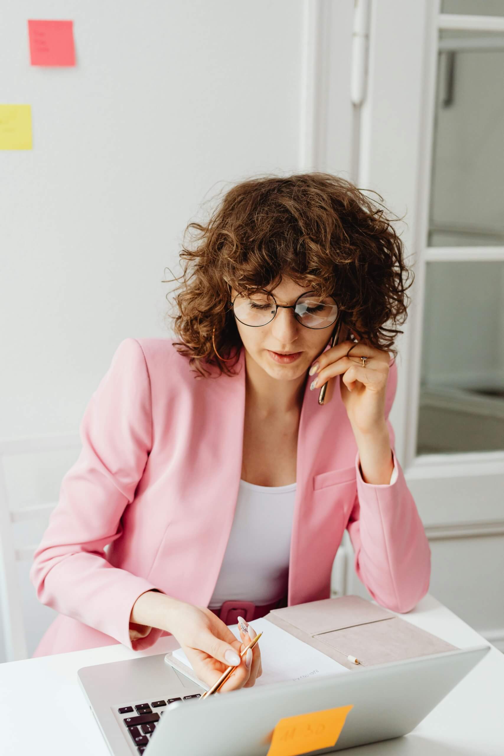 Woman in pink blazer thoughtfully working indoors.