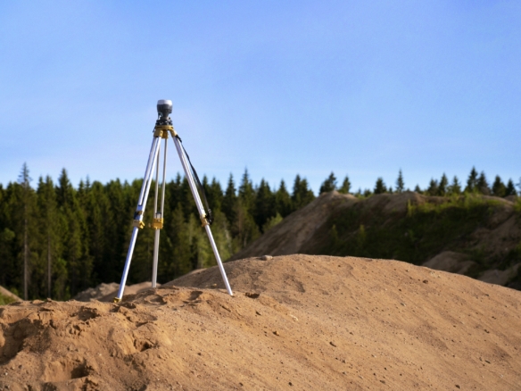 Surveying equipment set up on a mound of dirt with trees and sky in the background.