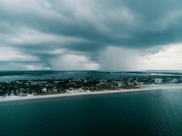 Storm clouds gather over a coastal town beside the ocean.
