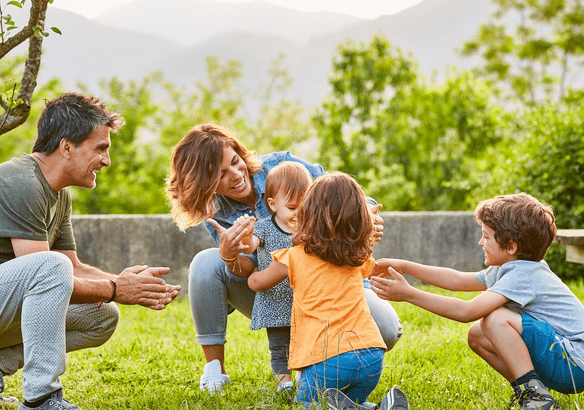 A joyful family playing with a toddler outdoors in a green field.