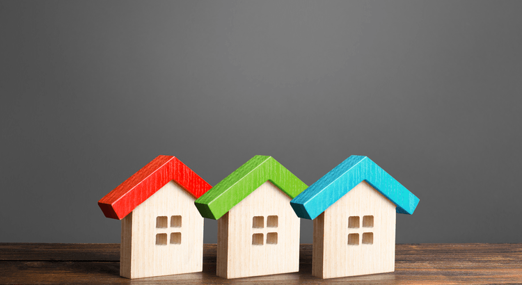Three small wooden houses with colorful roofs on a grey background.