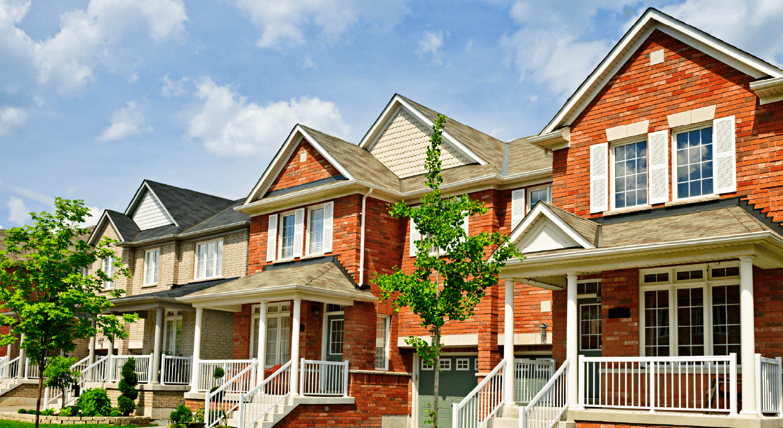 Row of charming red brick houses with white porches and green trees.