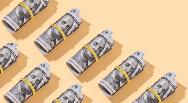 Rolled dollar bills on peach background.